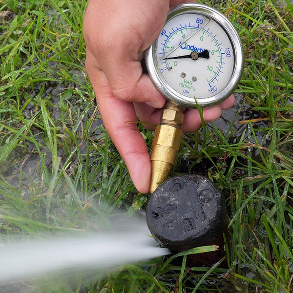 Handheld pressure gauge measuring nozzle pressure in Miami-Dade County bermudagrass soccer field.